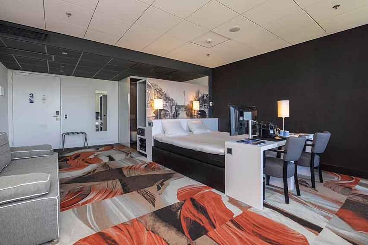 Ein Hotelzimmer mit einem Bett, einem Schreibtisch mit Stuhl, einer Couch und einem gemusterten Teppich.