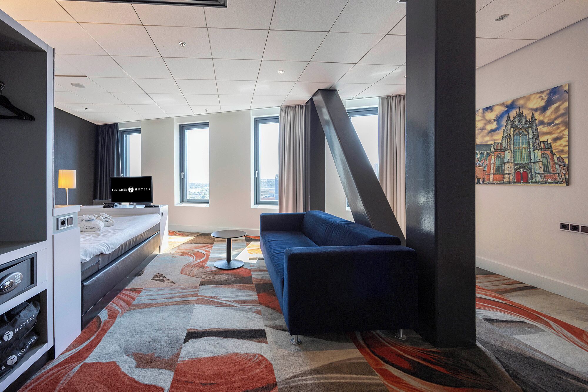 Ein Hotelzimmer mit Bett, einer Couch, einem Fernseher, einem Schreibtisch und einem Bild an der Wand.