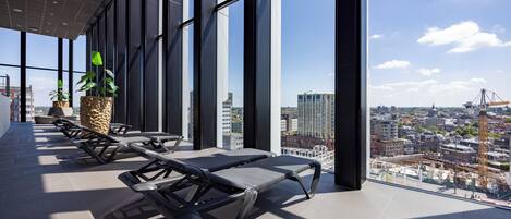 A modern lounge area with large windows, sun loungers, and potted plants.