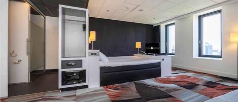 A modern hotel room with a bed, a desk, a chair, a TV, and a large window.