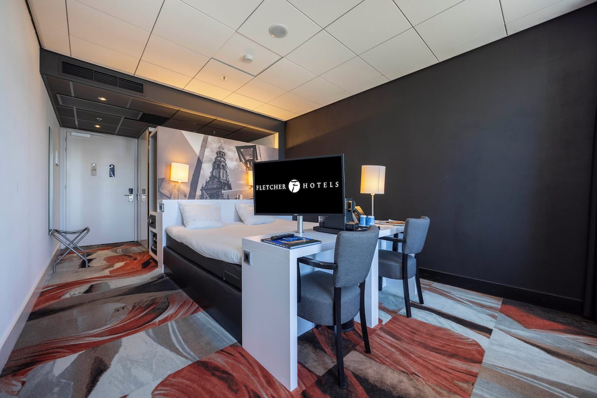 Ein Hotelzimmer mit Bett, Schreibtisch, Stuhl und einem Flachbildfernseher.
