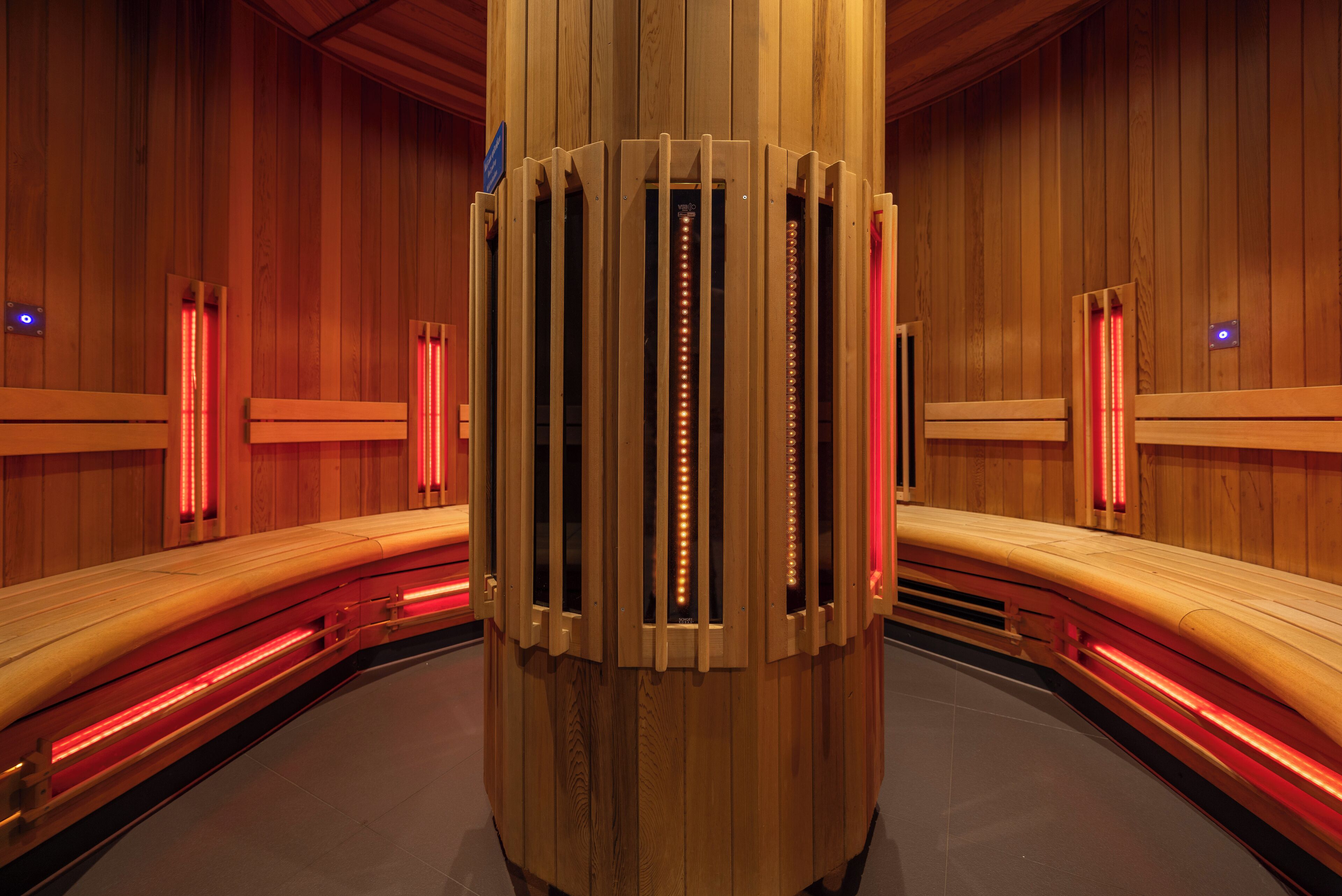 A sauna with wooden benches and a central pillar with lights.