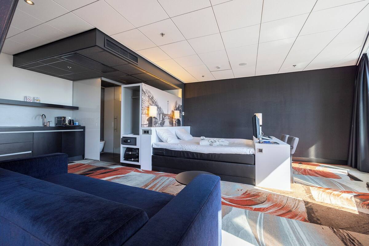 Ein modernes Hotelzimmer mit Bett, Schreibtisch, einer Sitzecke und einem Blick auf die Stadt.