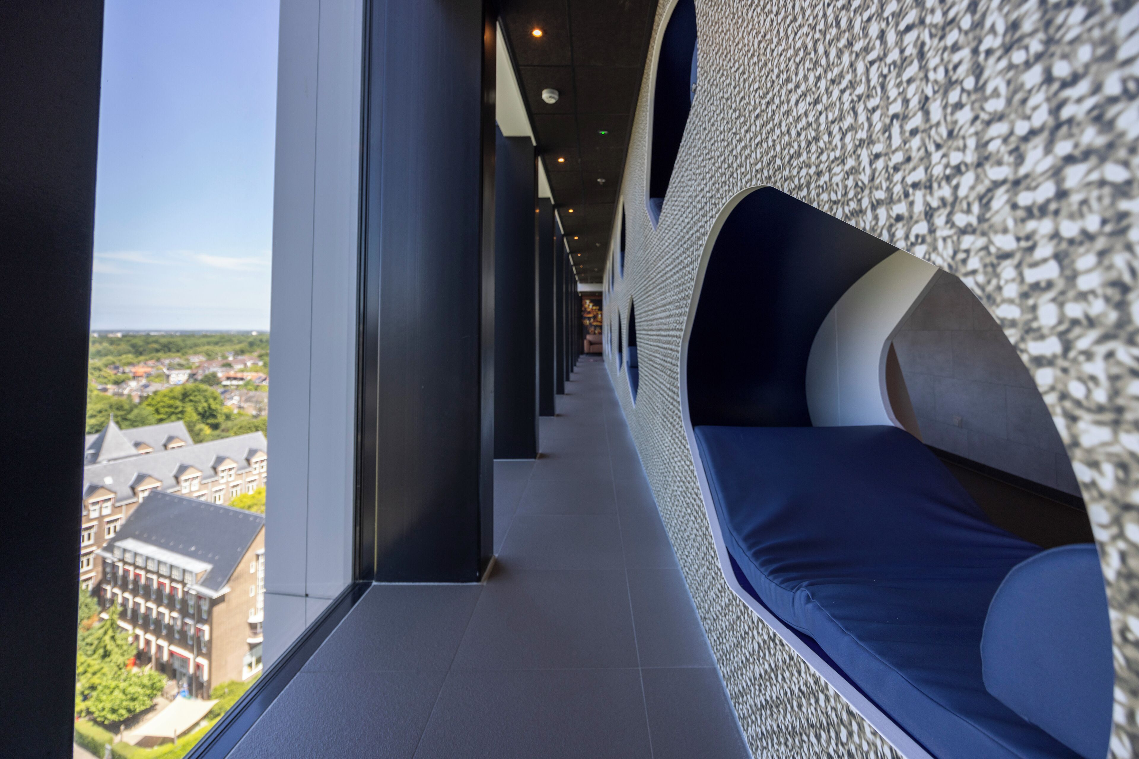 A corridor with a view of buildings, a patterned wall, and a blue bench.