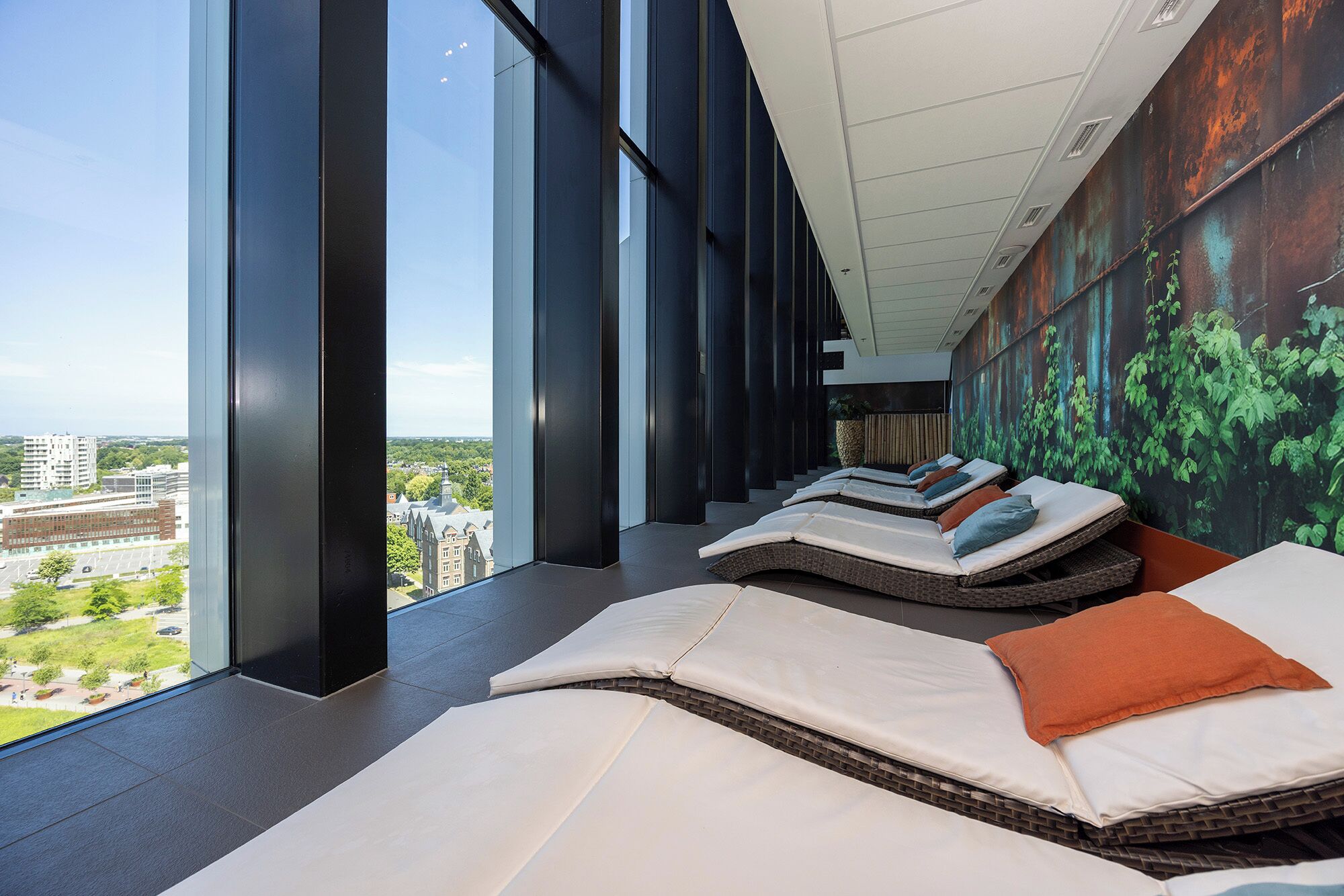 Een moderne spa-ruimte met grote ramen, verstelbare fauteuils en een bosdecoratie op de muur.