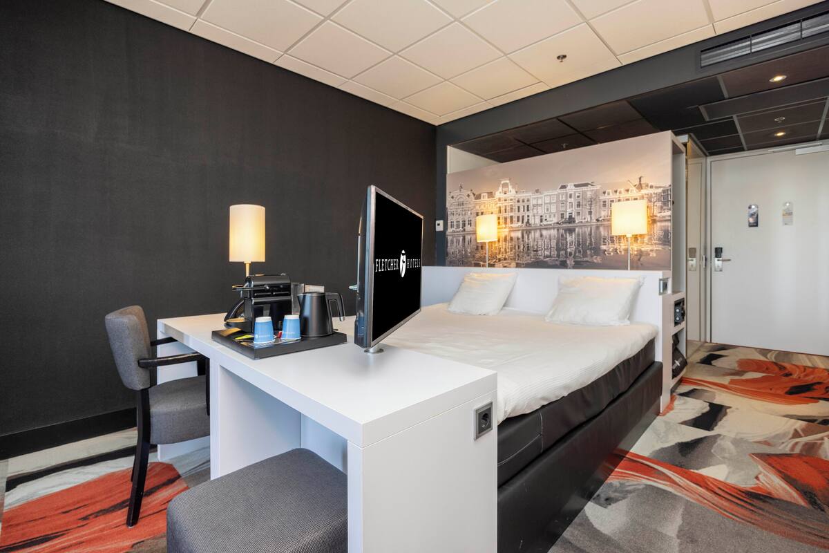 Ein Hotelzimmer mit einem Bett, einem Schreibtisch mit Computer, einem Sessel, einer Kaffeemaschine und einer Lampe.