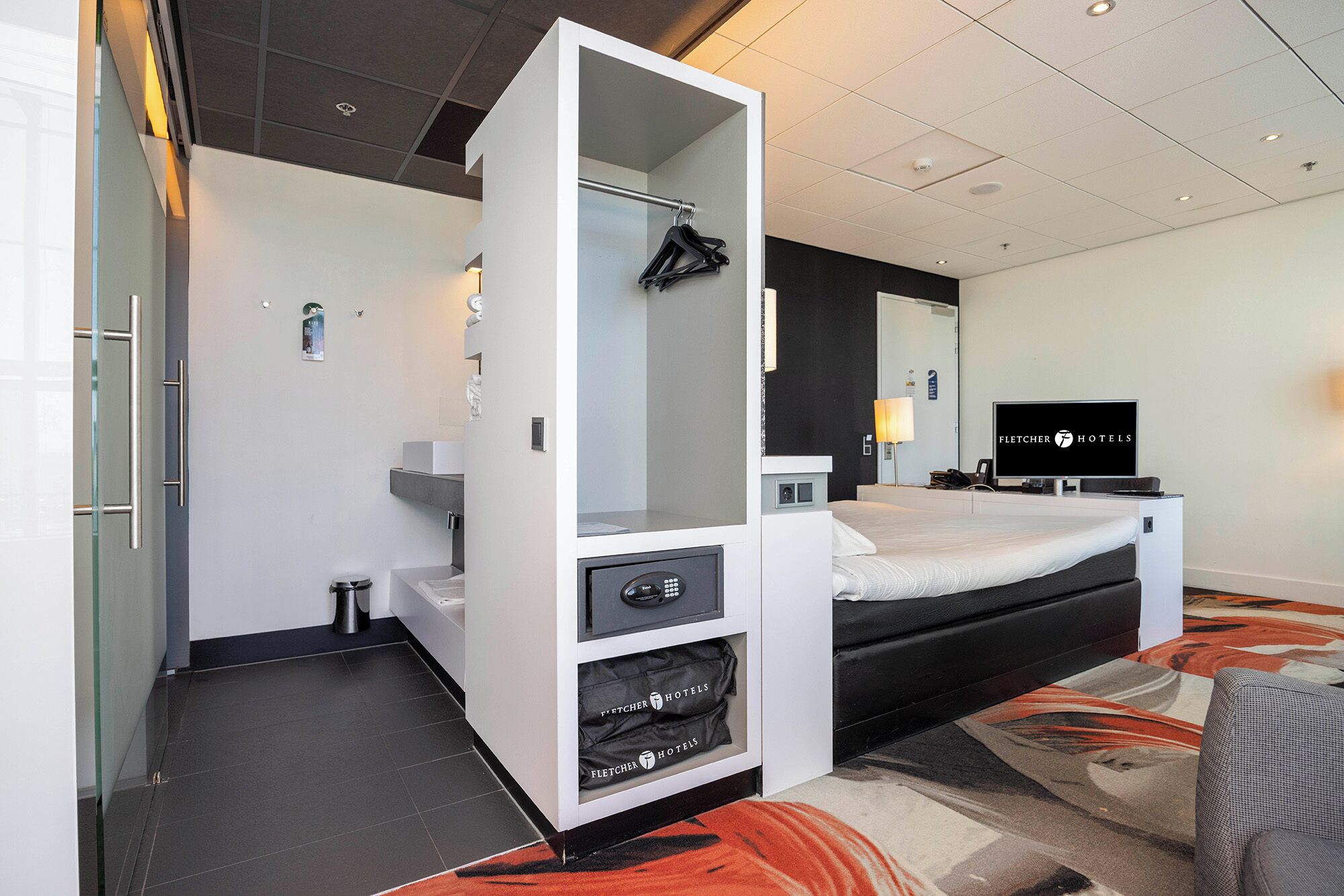 Een moderne hotelkamer met een bed, een televisie, een minibar en een badkamer.