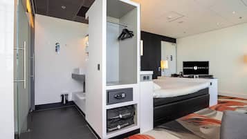 Een moderne hotelkamer met een bed, een televisie, een minibar en een badkamer.