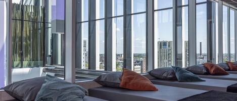 A modern interior with large windows, seating areas with cushions, and a view of the cityscape.