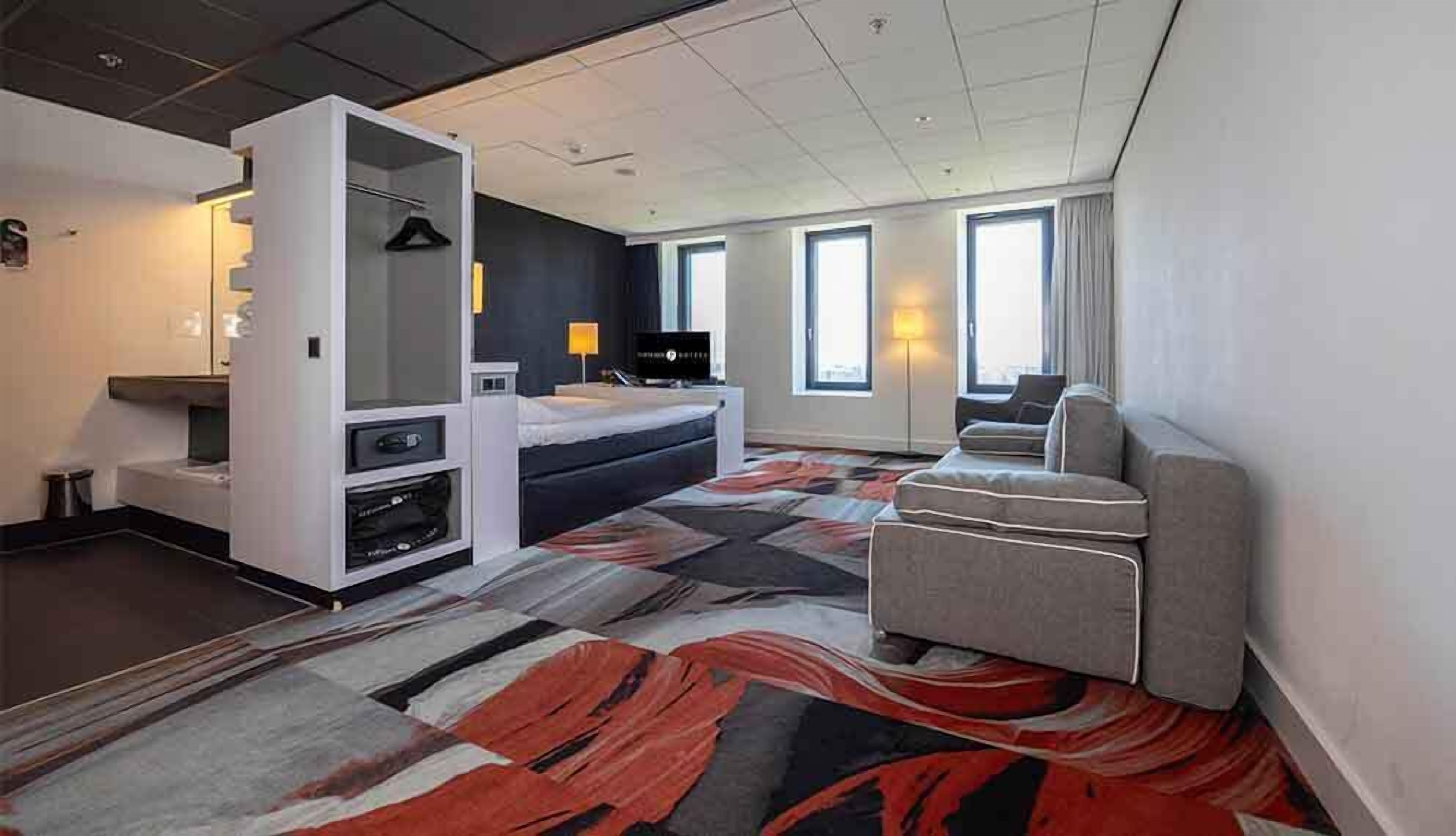 A modern hotel room with a bed, a sofa, a desk, and a TV.