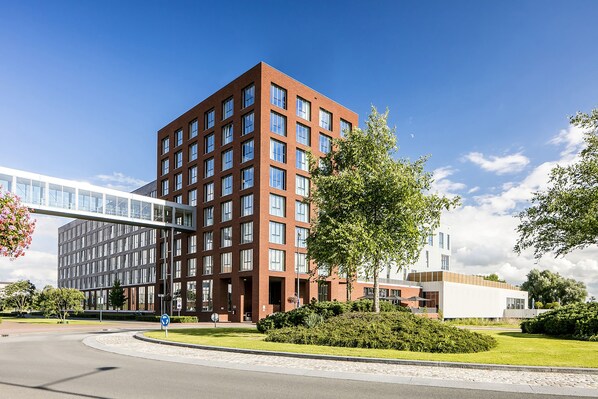 A modern building with a glass facade, a brick structure, and a pedestrian bridge. - Fletcher Wellness - Hotel Helmond (Helmond)