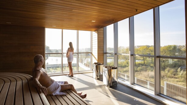 Un sauna con bancos de madera y ventanas amplias que dan vistas a árboles y un cuerpo de agua.
