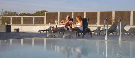Zona junto a la piscina con sillones de descanso y una piscina cristalina.