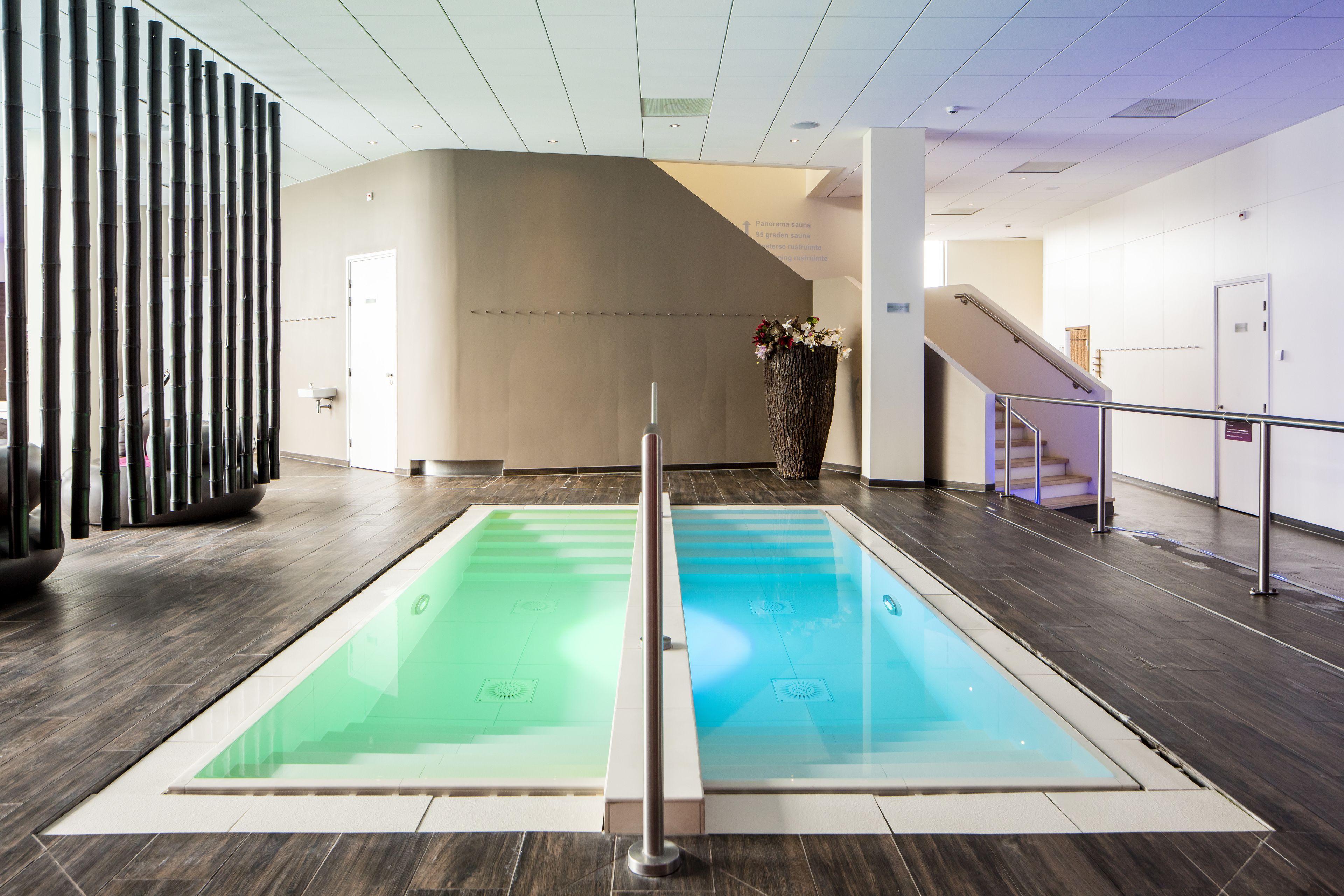 Zona d'una piscina interior moderna amb dues piscines, una escala i una recepció.
