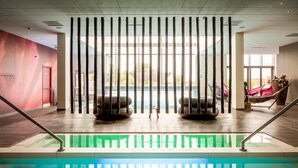 Una piscina con fondo de cristal, rodeada por un interior moderno con una pared roja y un ventanal grande.