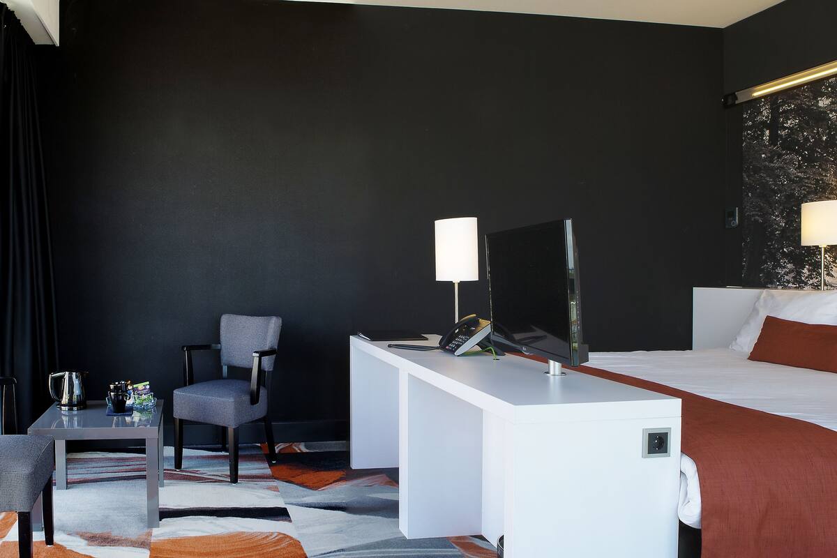 A hotel room with a bed, a desk, a chair, and a cityscape mural on the wall.