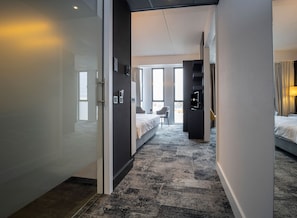 A hotel corridor with a bed, a TV, and a desk. - Fletcher Wellness - Hotel Helmond (Helmond)