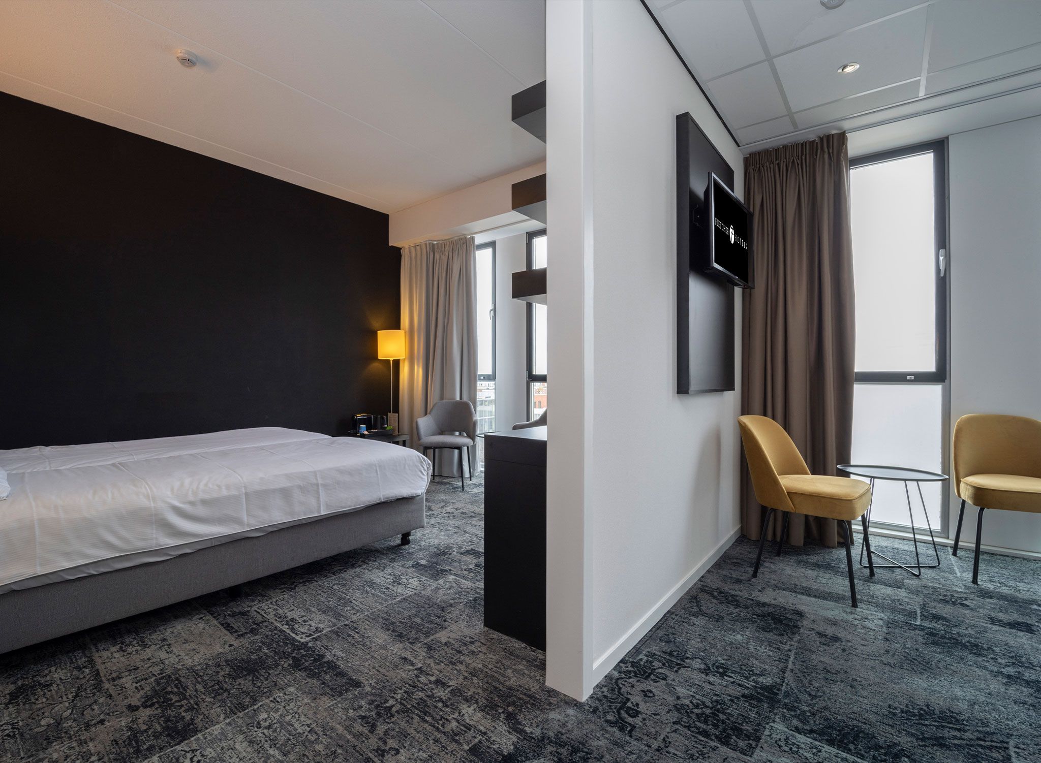Ein Hotelzimmer mit Bett, Schreibtisch, Stuhl, Fernseher und Blick auf die Stadt.