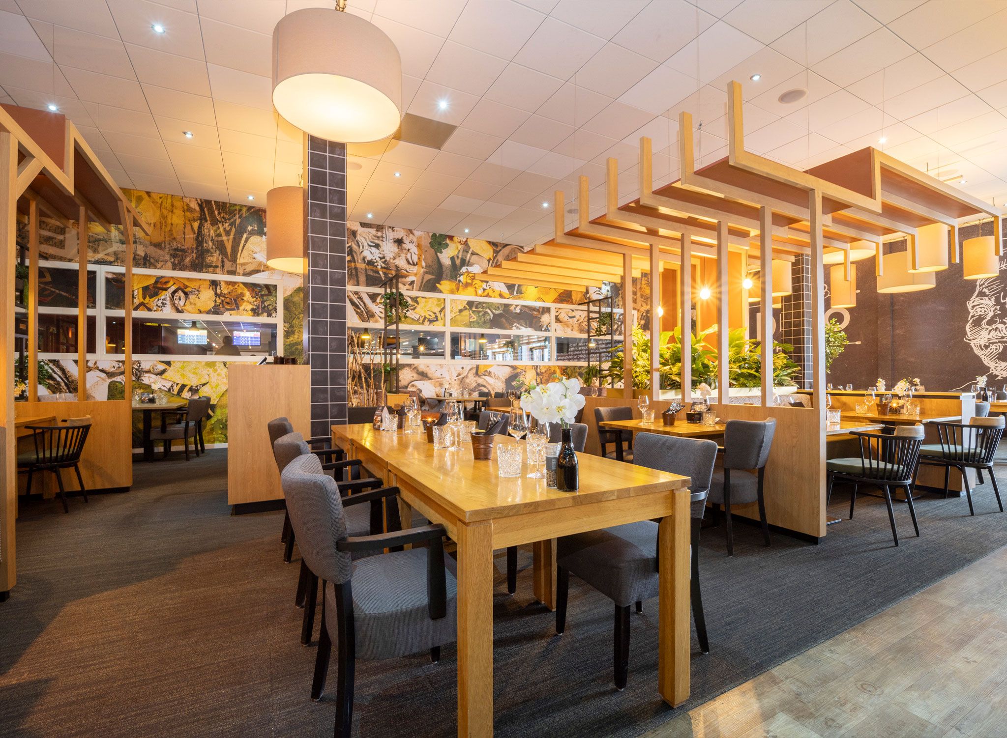 A restaurant with a long wooden table, multiple chairs, and a high ceiling with recessed lighting.
