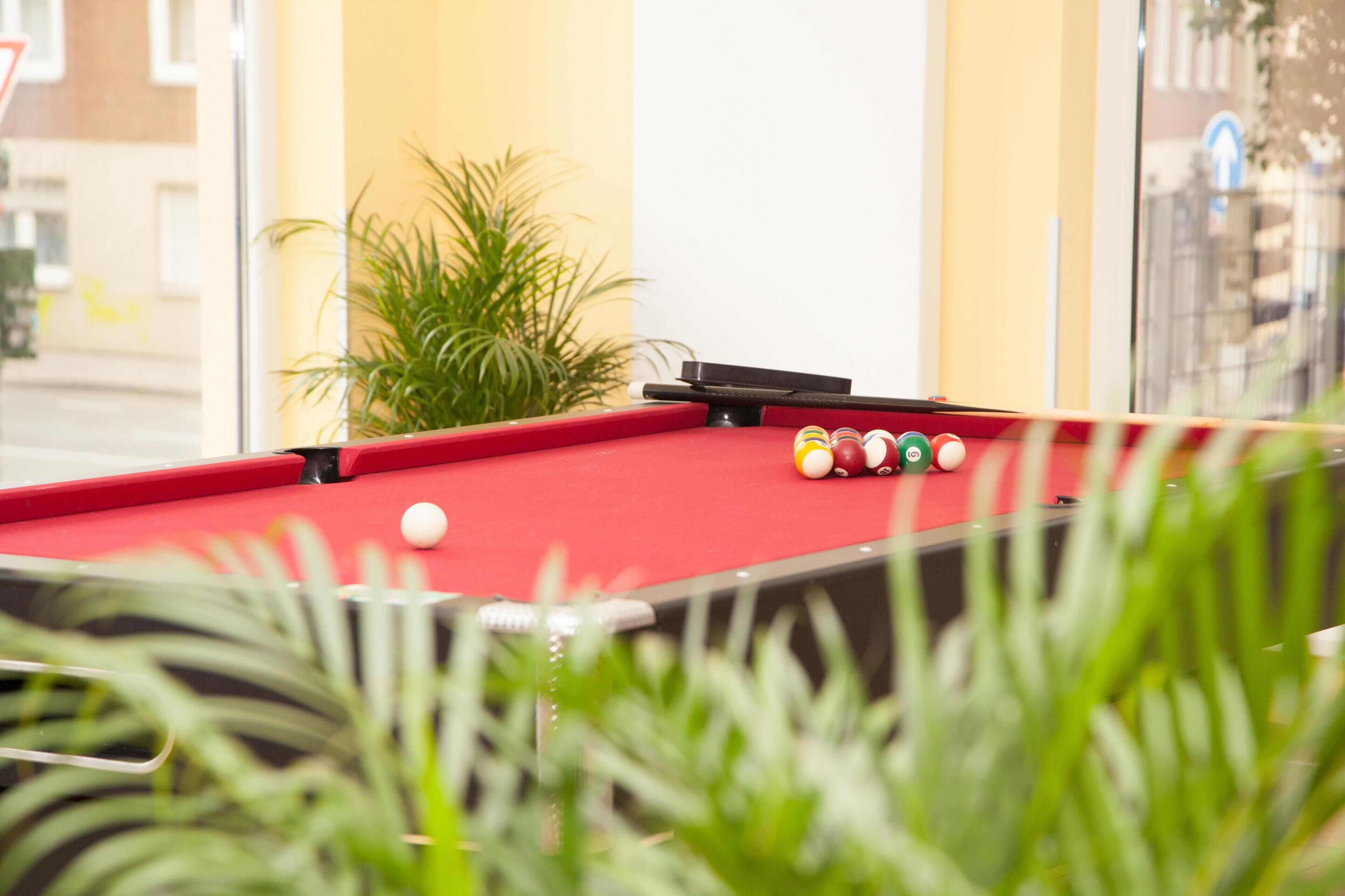 Une table de billard avec des billes et une queue, entourée de plantes vertes.