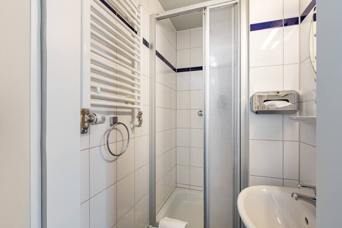 Un baño con ducha, lavabo y un perchero para toallas.