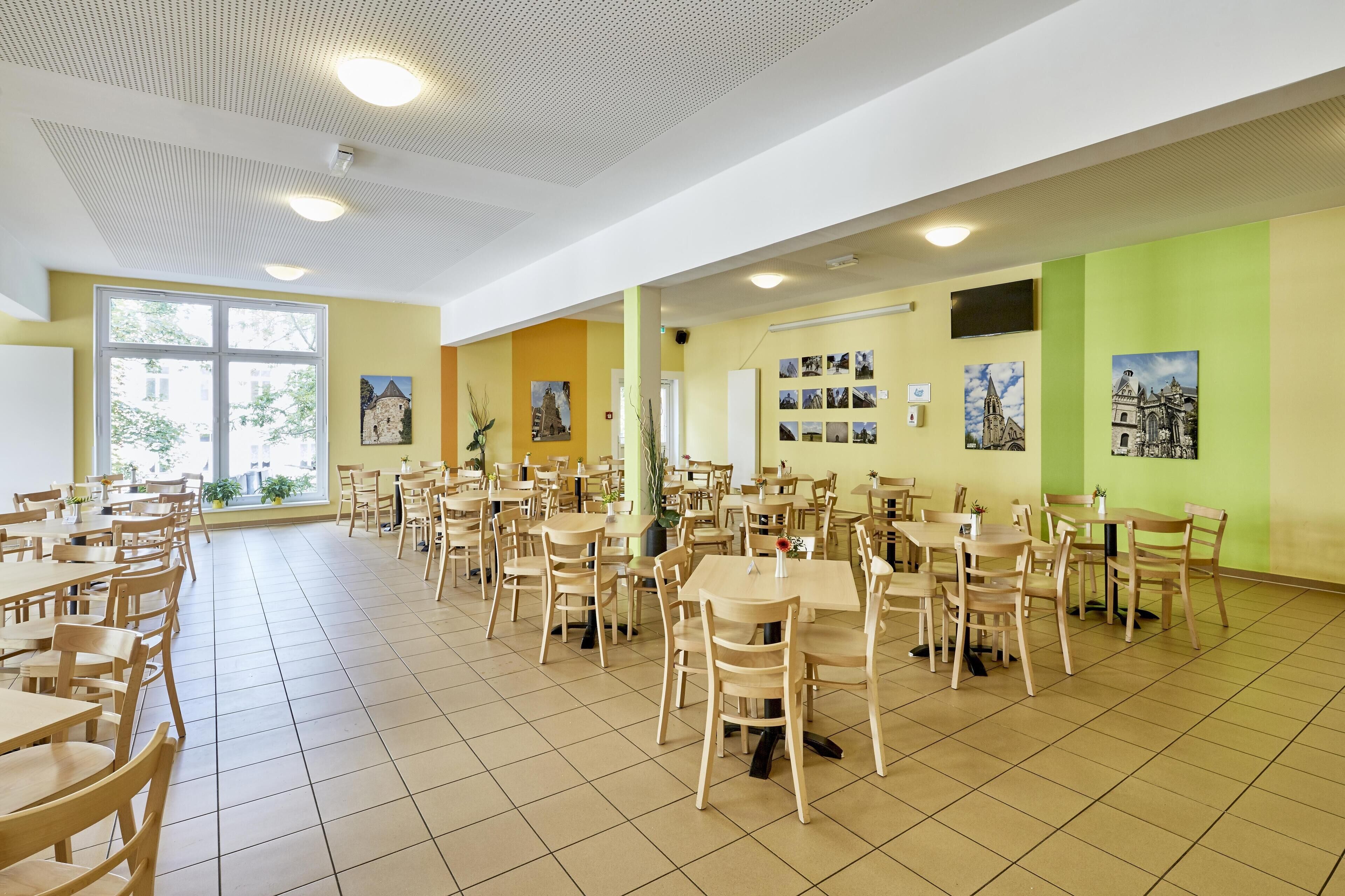 Un vaste espace dédié à la salle à manger, comprenant plusieurs tables et chaises, de grandes fenêtres et des tableaux accrochés aux murs.