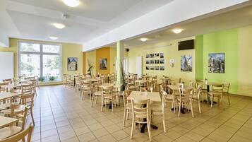 Un vaste espace dédié à la salle à manger, comprenant plusieurs tables et chaises, de grandes fenêtres et des tableaux accrochés aux murs.