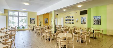 Un comedor espacioso con varias mesas y sillas, ventanas amplias y cuadros colgados en la pared.