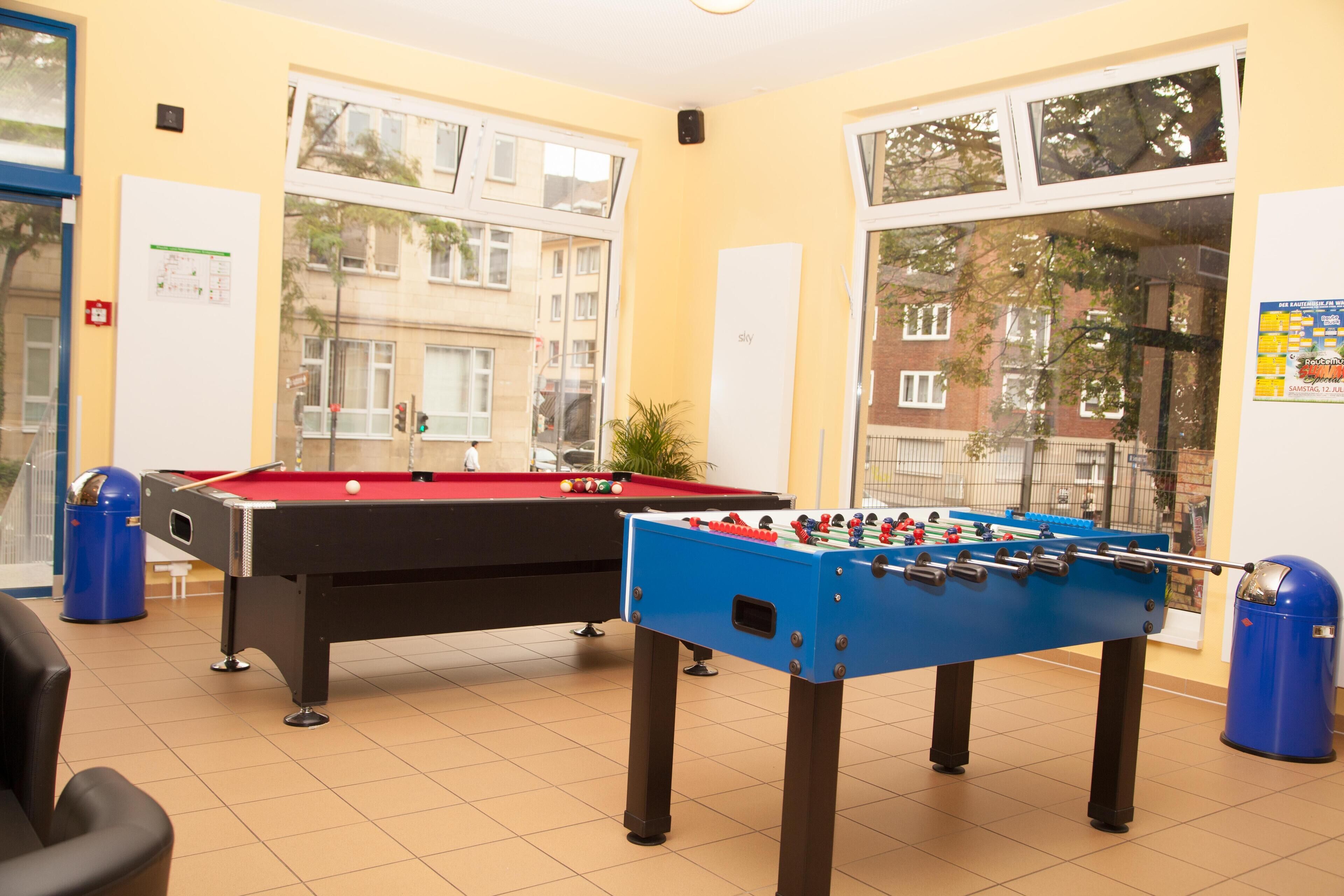 A room with two foosball tables, a pool table, and a trash bin.