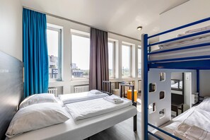 Habitación de hotel con literas, una cama individual y vistas a la ciudad a través de amplias ventanas.