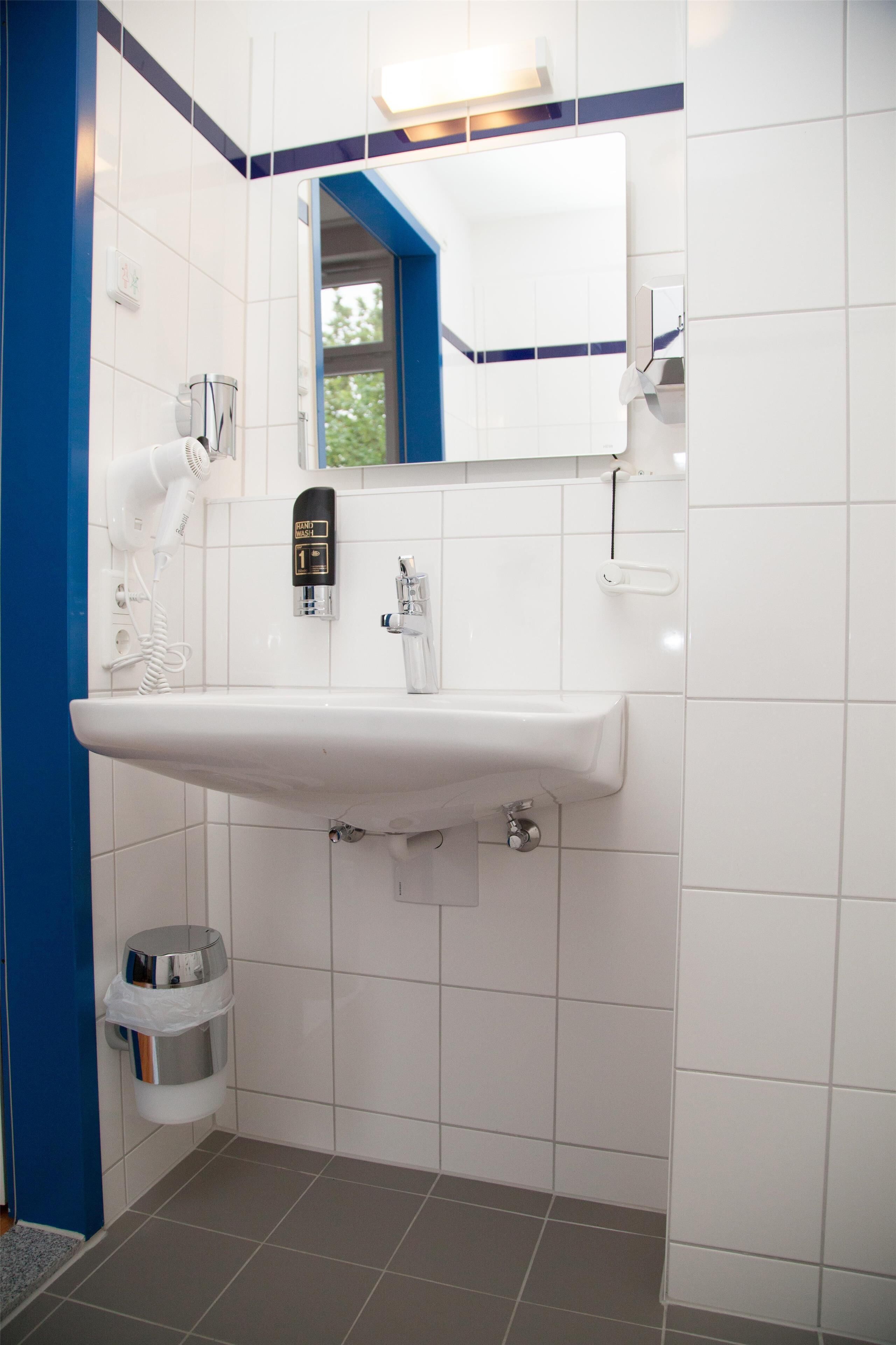 A modern bathroom with a white sink, a mirror, and a hairdryer.