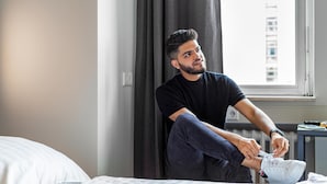 Una persona sentada en una cama, atándose un zapato.