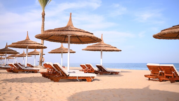 Ein Strand mit Liegestühlen aus Holz und Reetdachschirmen.