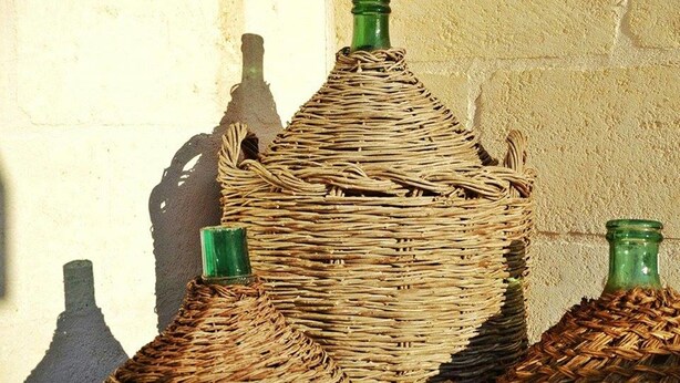 A wicker basket with a green bottle inside, placed against a textured wall. - Agriturismo I Pozzetti (Fasano)