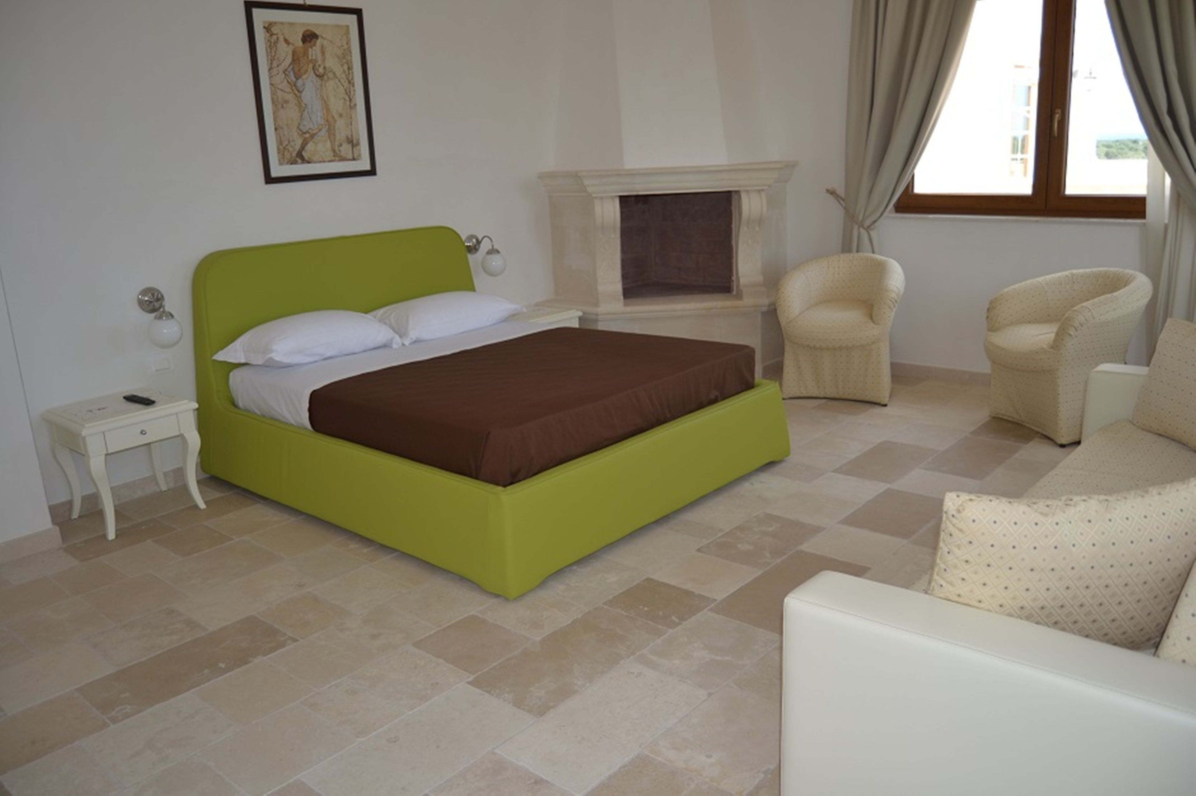 A bedroom with a green bed, a white nightstand, a fireplace, and two armchairs.