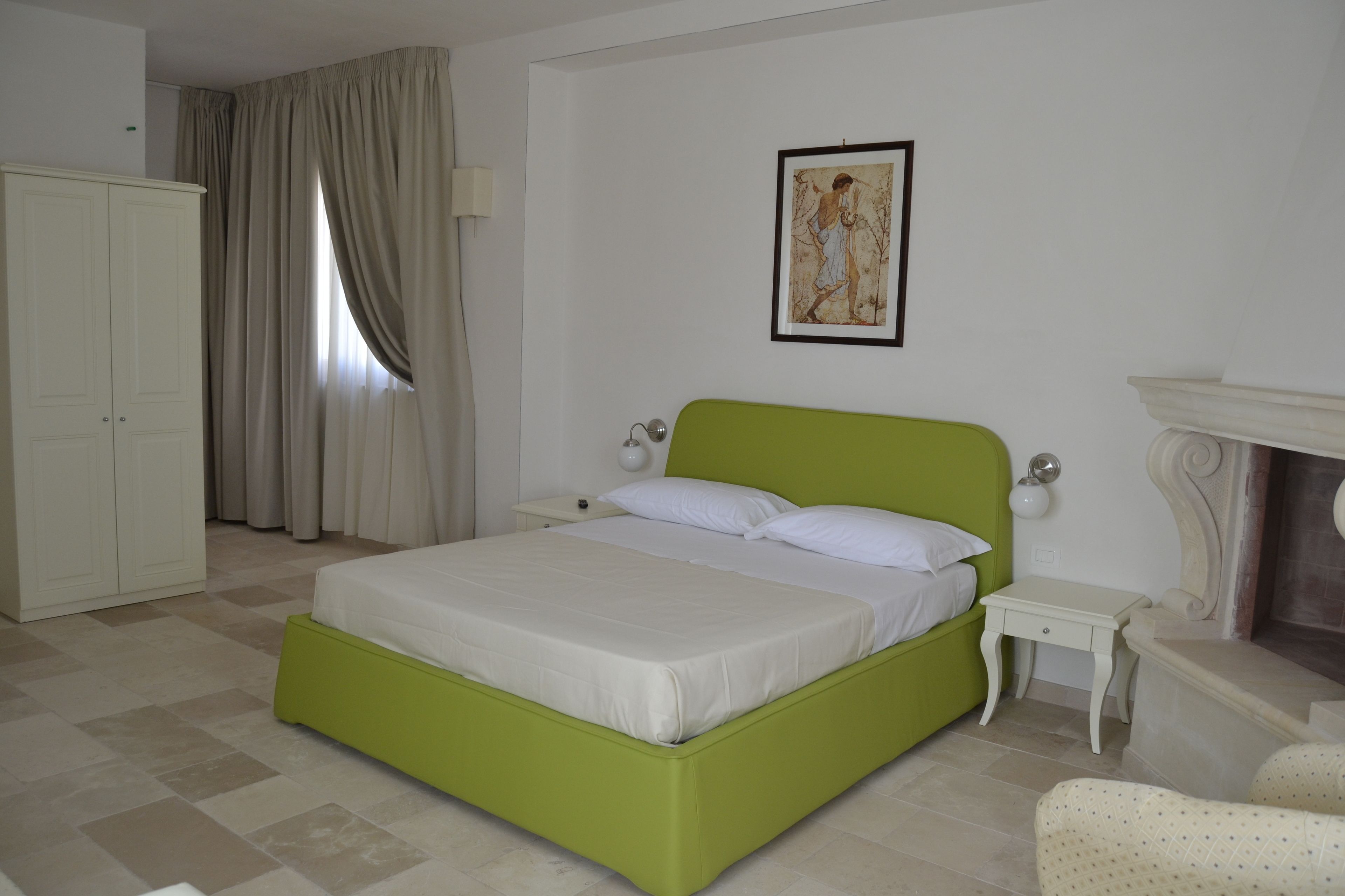 Una camera da letto con un letto verde, tende bianche, un quadro appeso al muro, un comodino e una sedia.