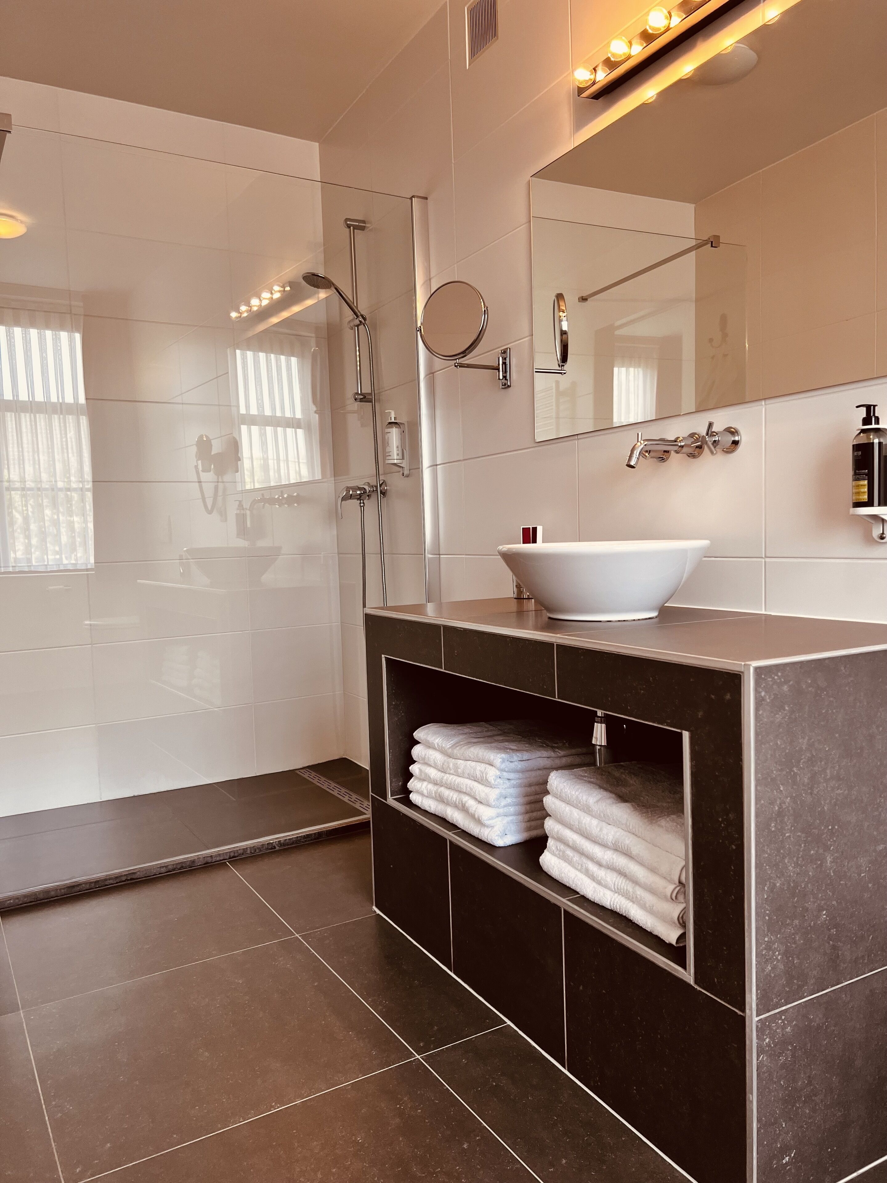 A modern bathroom with a large mirror, a white sink, a shower with a handheld showerhead, and a towel rack.