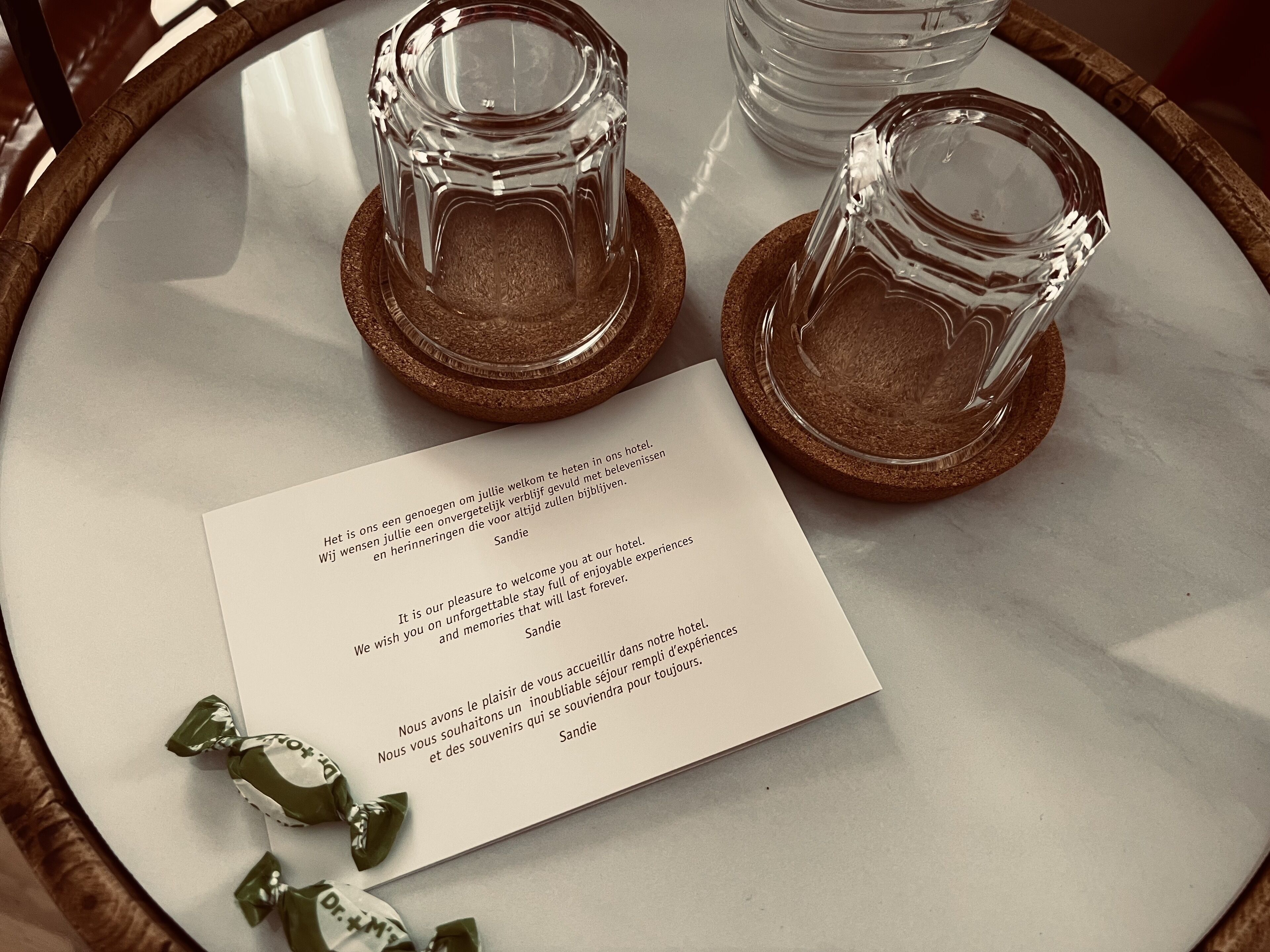 A welcome card on a marble table with two clear glasses on coasters.