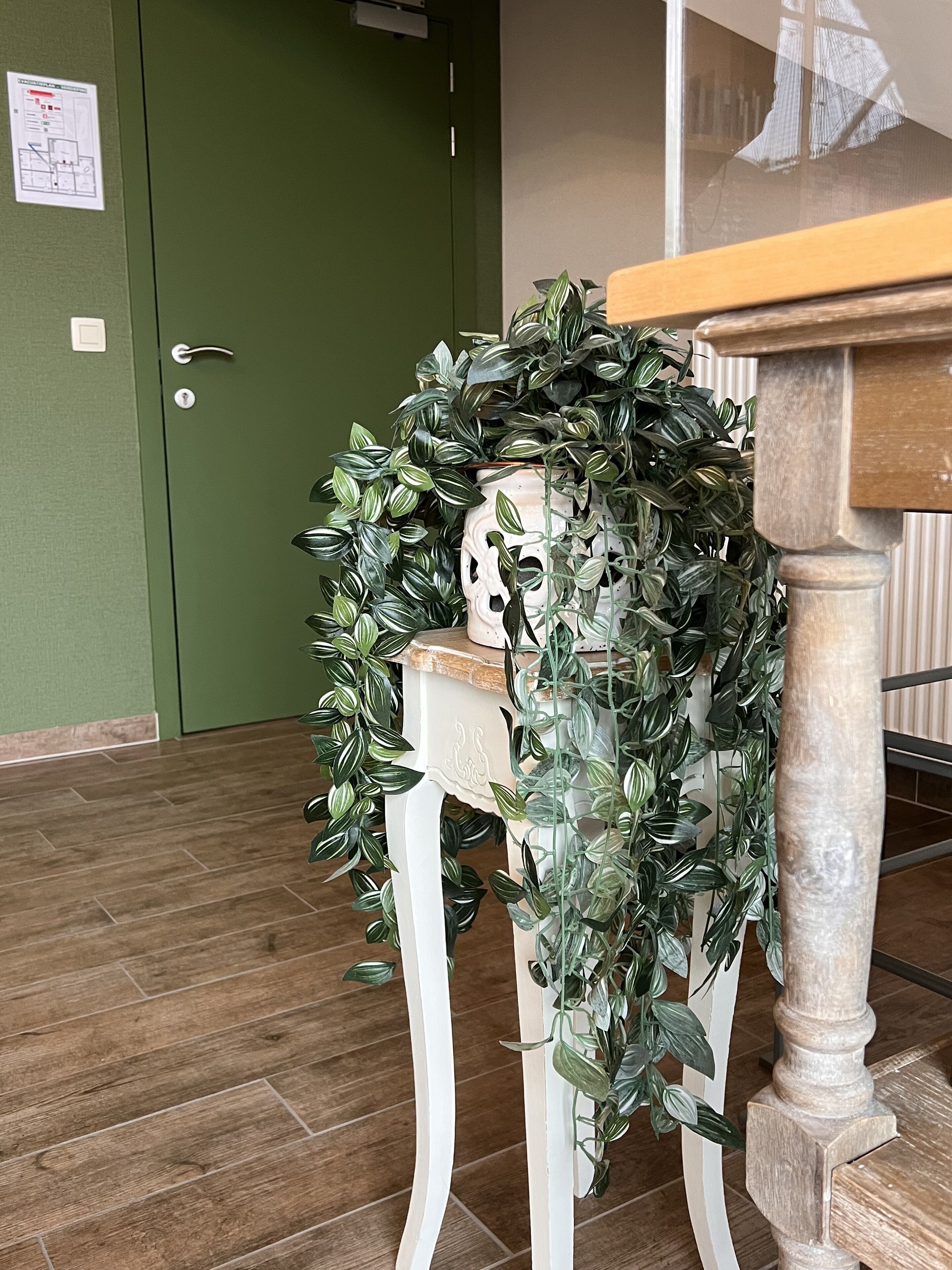 Una silla blanca con una planta verde enroscada, una mesa de madera y una puerta verde con un picaporte blanco.