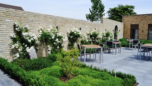A courtyard with stone walls, white flowering plants, and outdoor seating. - Hotel Het Heilig Genot (Vleteren)