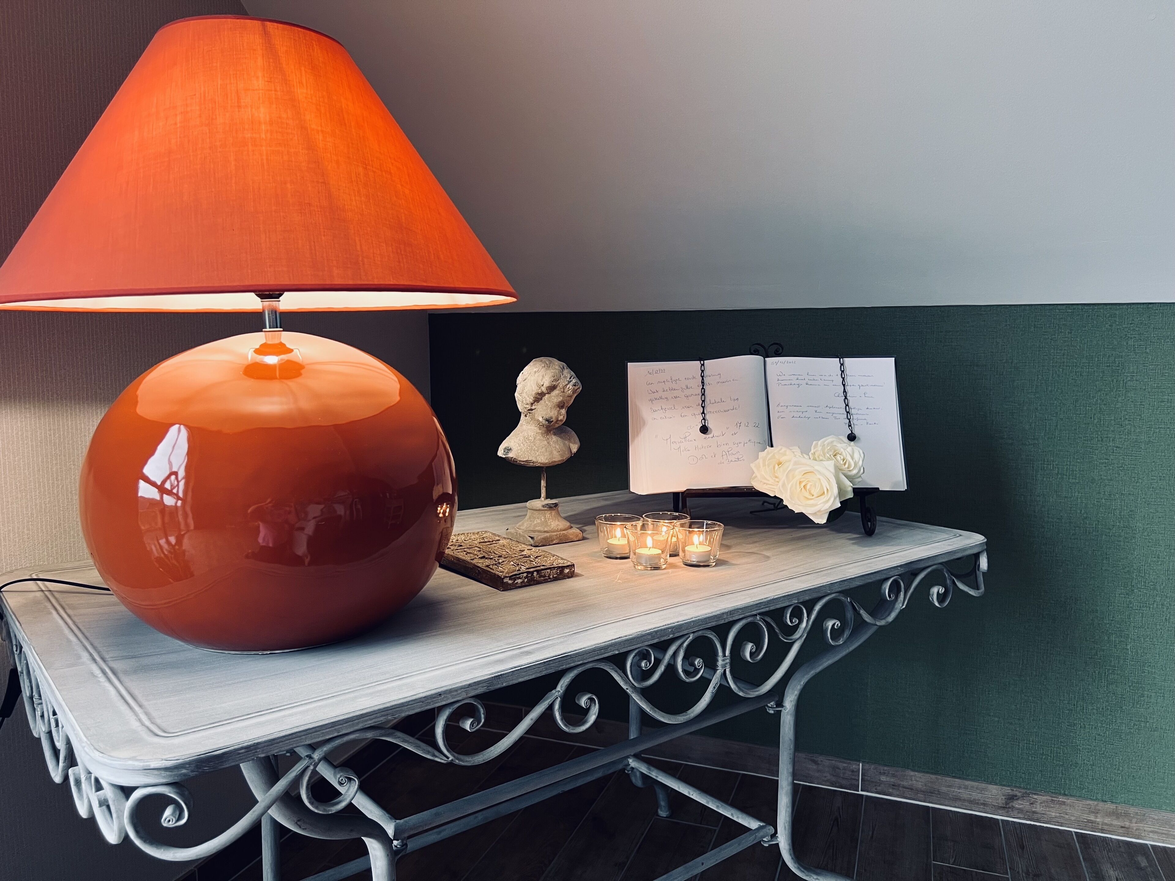 A table with a large orange lamp, a bust sculpture, candles, and a menu board.