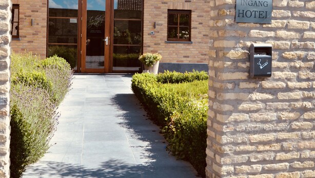 A brick building with a large arched entrance, a sign reading "INGANG HOTEL," and a pathway leading to the entrance. - Hotel Het Heilig Genot (Vleteren)