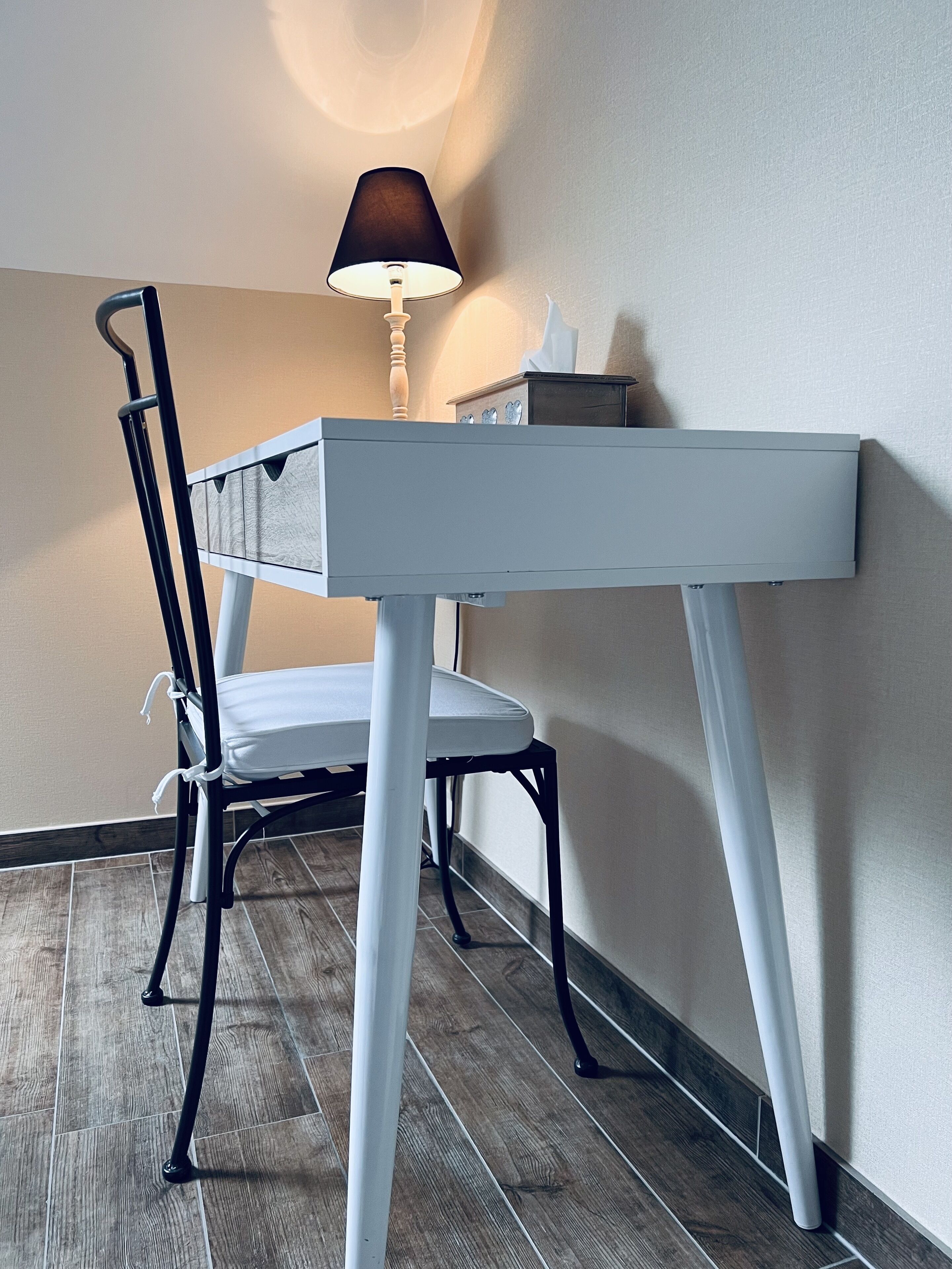 Ein weißer Schreibtisch mit einer Lampe, einem Stuhl und einer kleinen Schachtel darauf.
