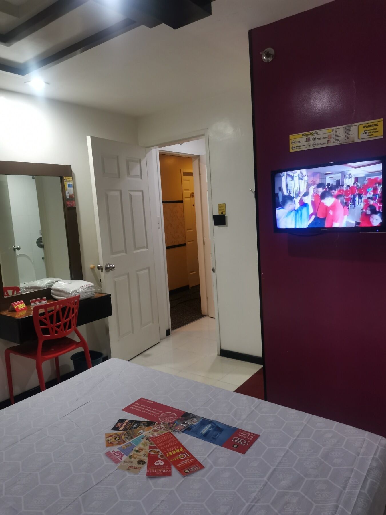 A hotel room with a bed, a TV, a desk with a chair, and a door leading to another room.