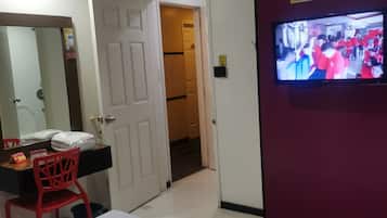A hotel room with a bed, a TV, a desk with a chair, and a door leading to another room.