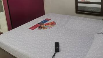 Una habitación de hotel con cama, televisor montado en la pared, una puerta roja y ventana con vistas al exterior.