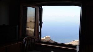 A room with a large window overlooking a coastal view, a wooden chair, and a small table. - Hotel Edelweiss (Erice)