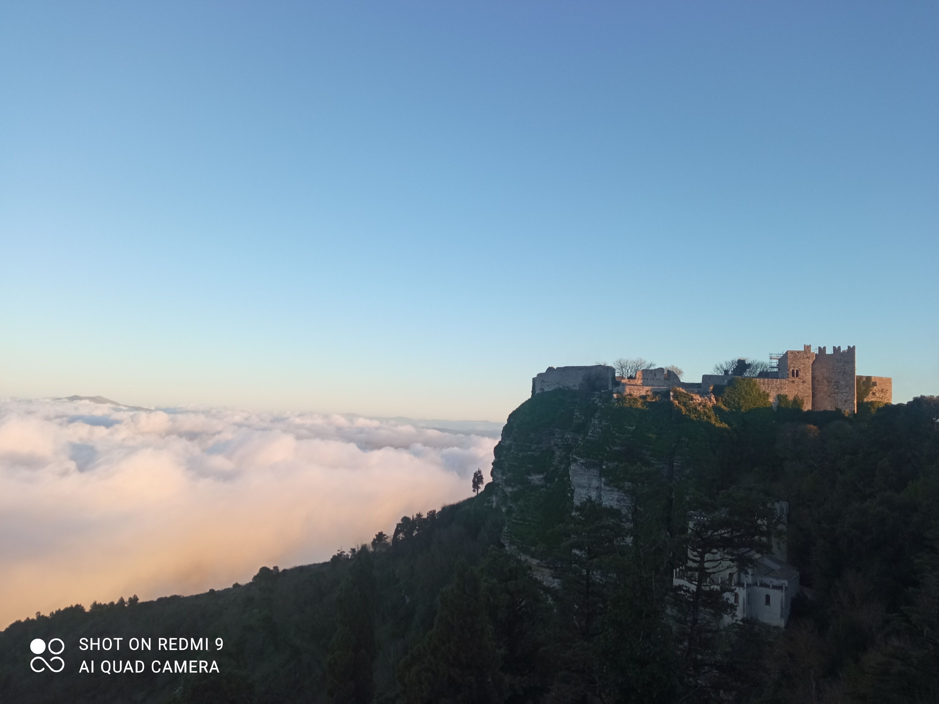 Un castillo en un acantilado con vistas a un valle de nubes.