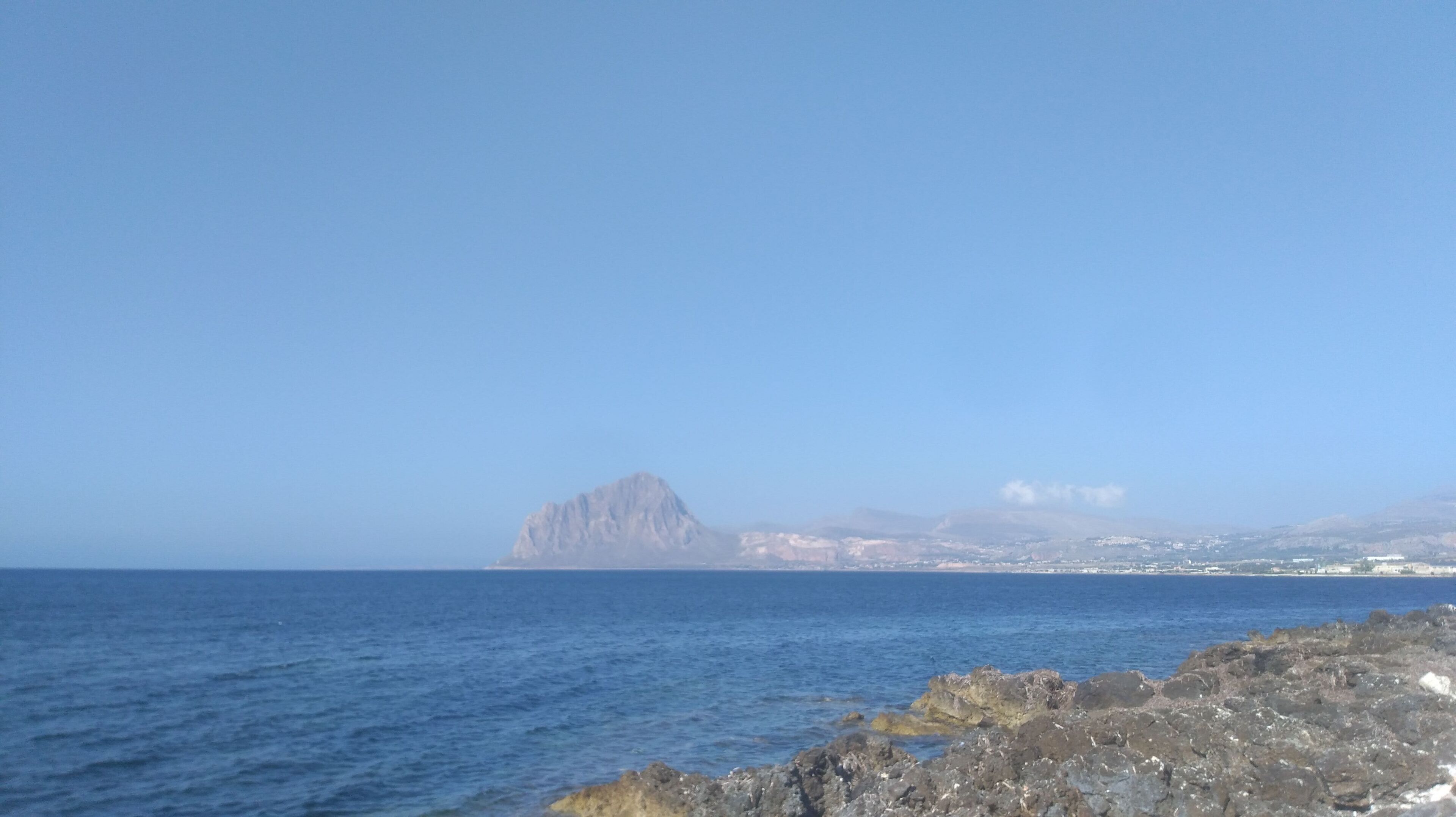 Un paysage côtier avec une rive rocheuse et une chaîne de montagnes à l’horizon.