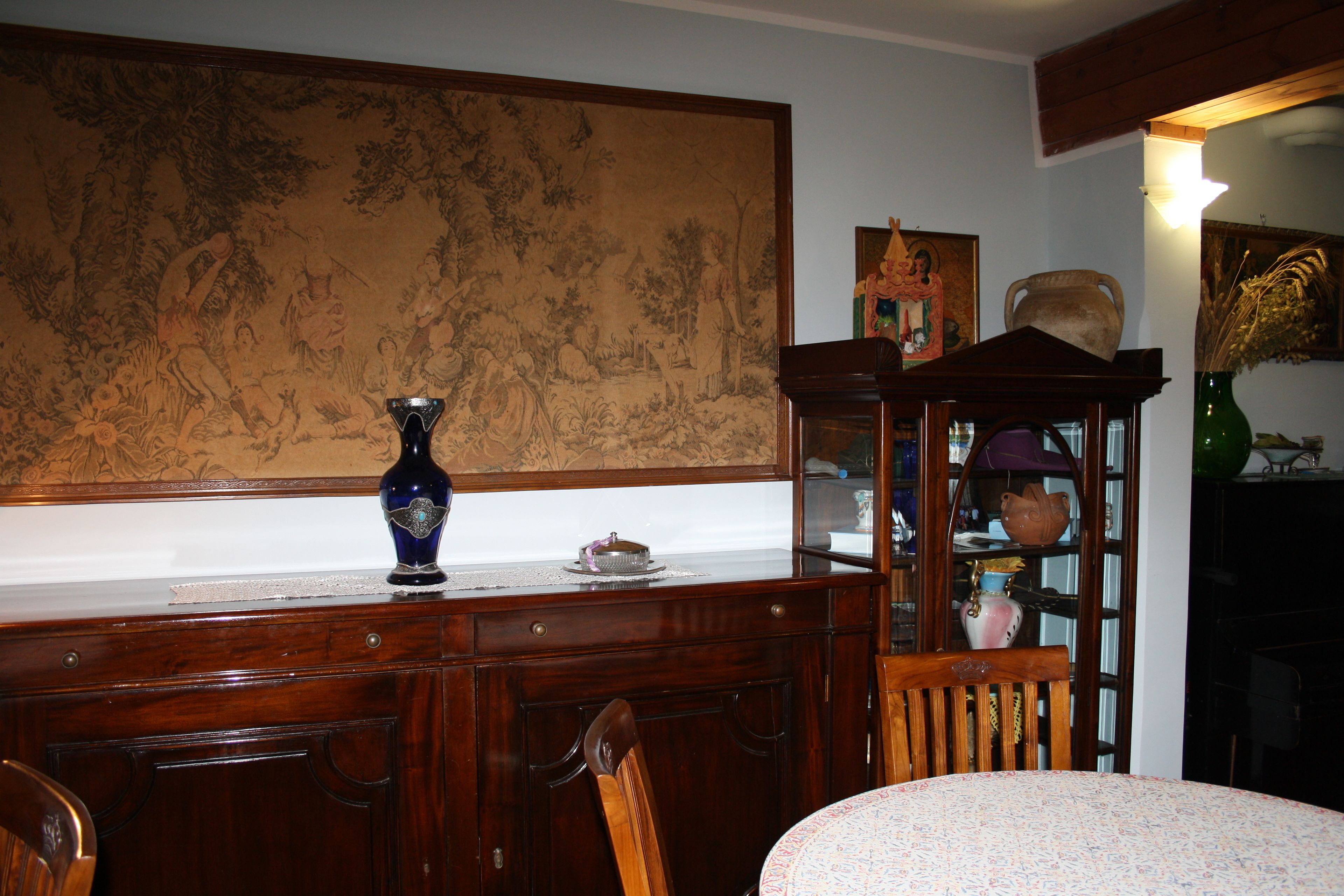 A wooden dining table with chairs, a vase, and a cabinet with glass doors.